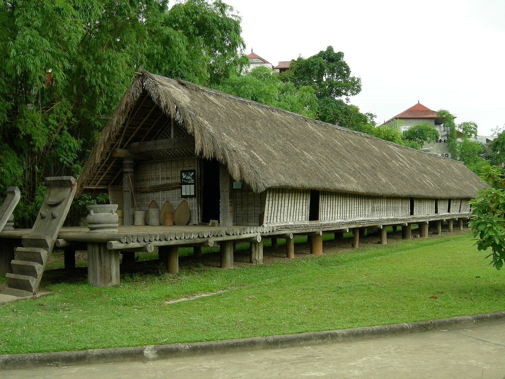 A Bahnar communal house with its tall thatched roof in the museum grounds