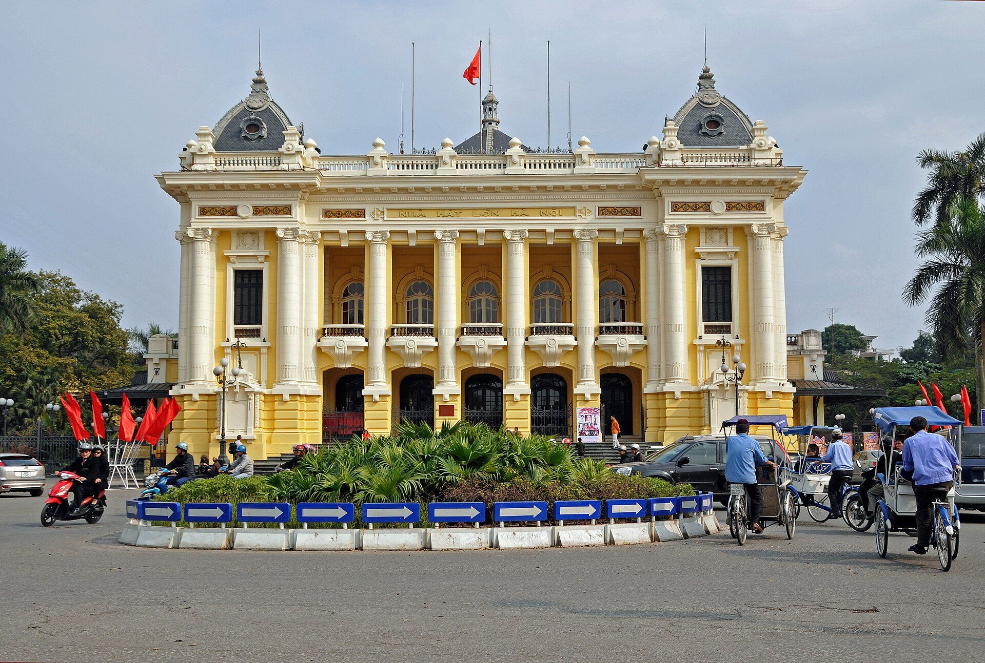 The Hanoi Opera House with flags flying and traffic crossing in front of it