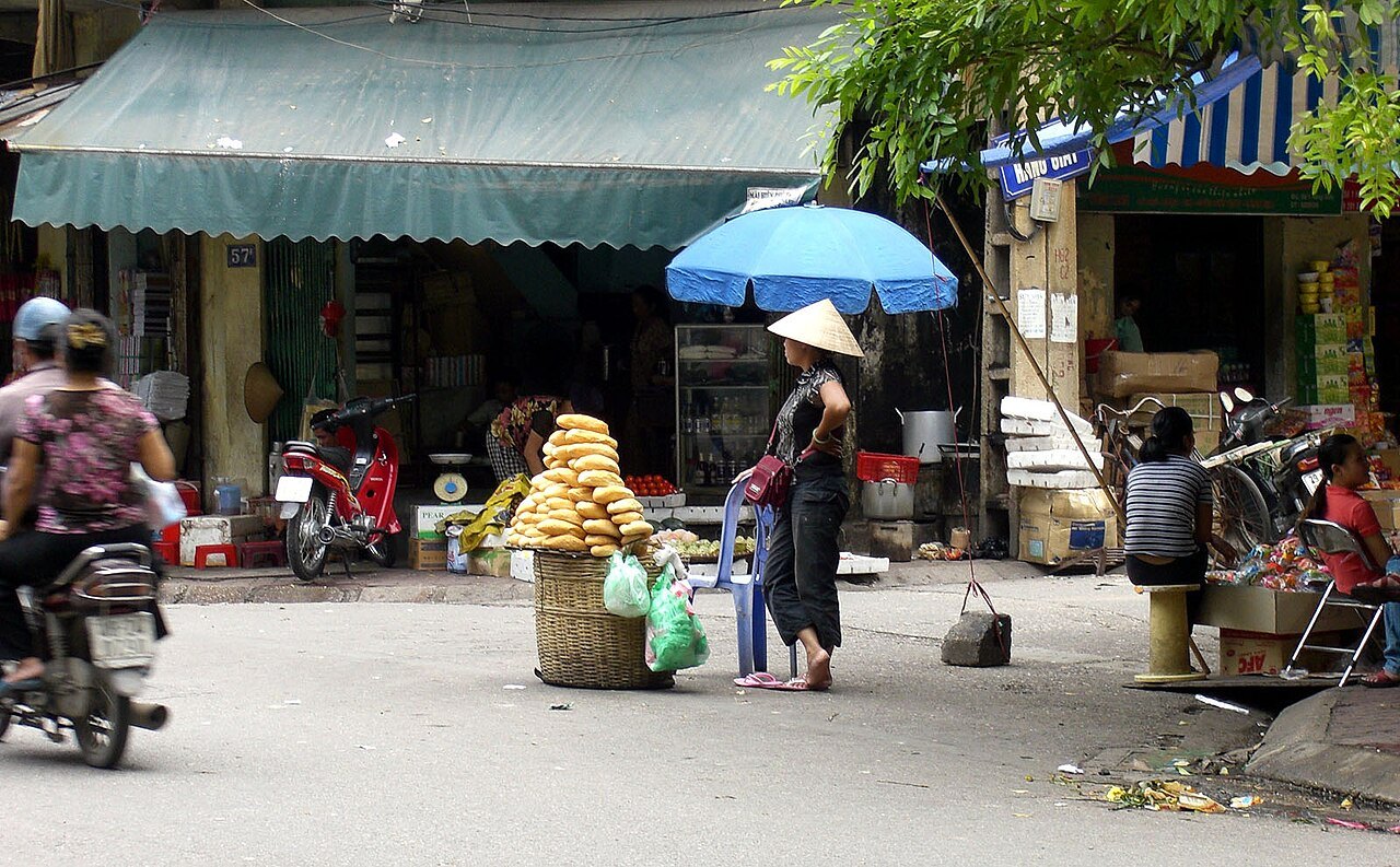 A bread seller under a blue umbrella outside a pavement shop in the French Quarter