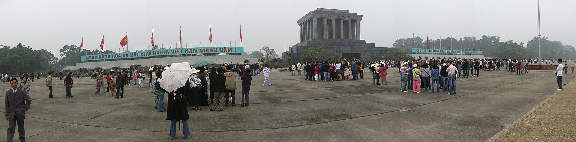 Ba Dinh Square with flags and visitors crossing the open paving