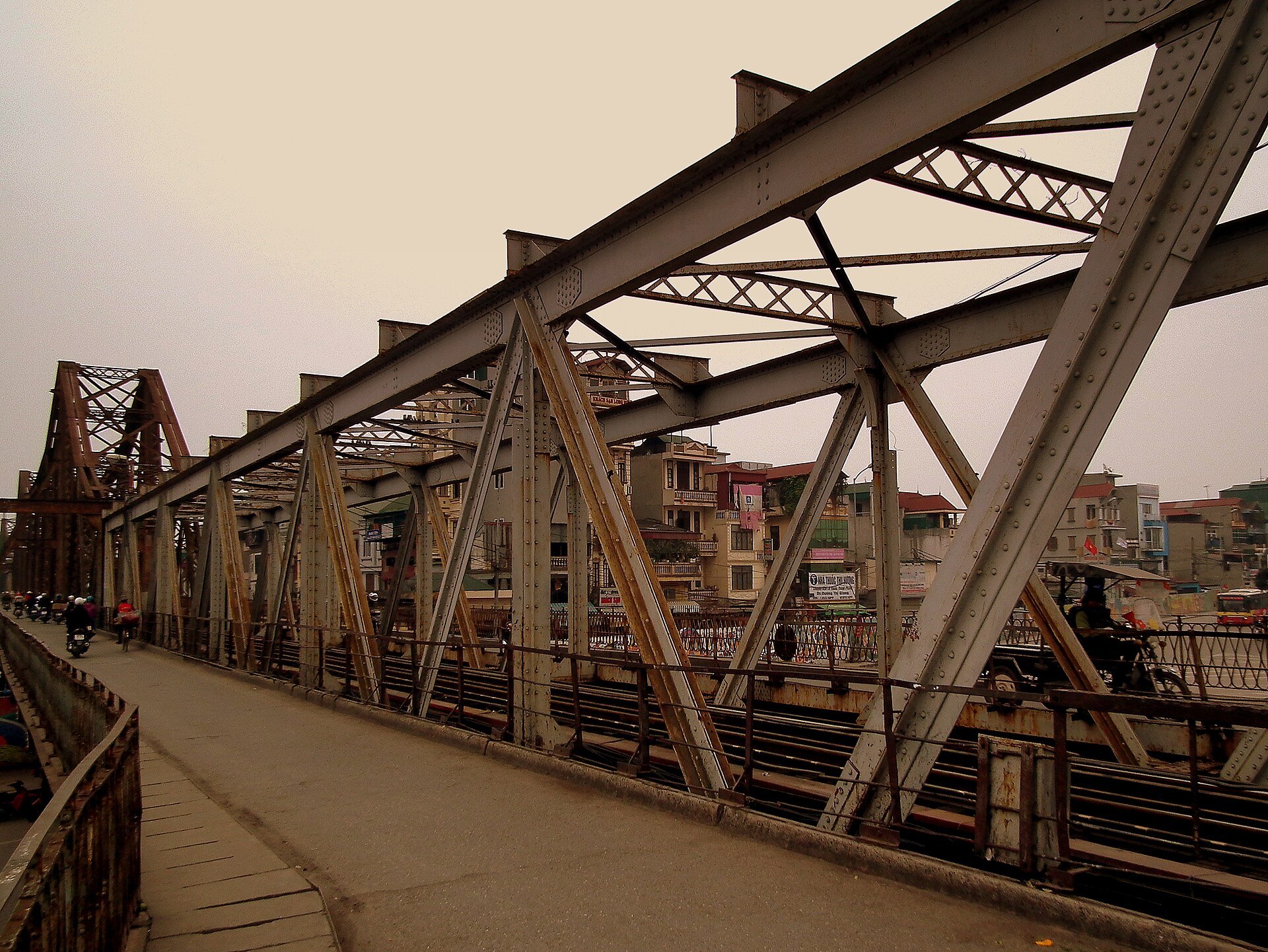 The riveted steel trusses of the Long Bien Bridge receding into the distance