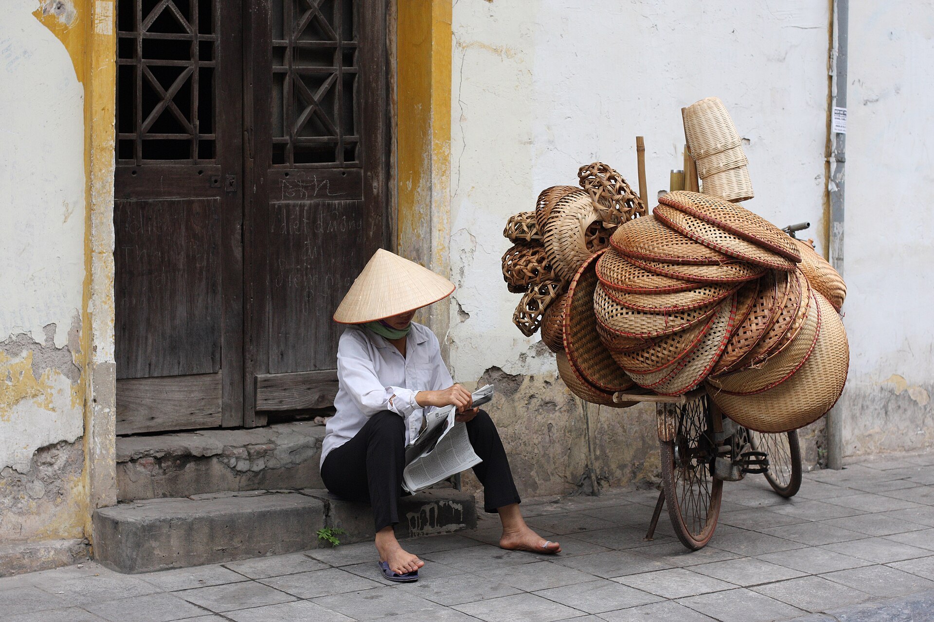 A street vendor with woven baskets stacked on her bicycle in the Old Quarter