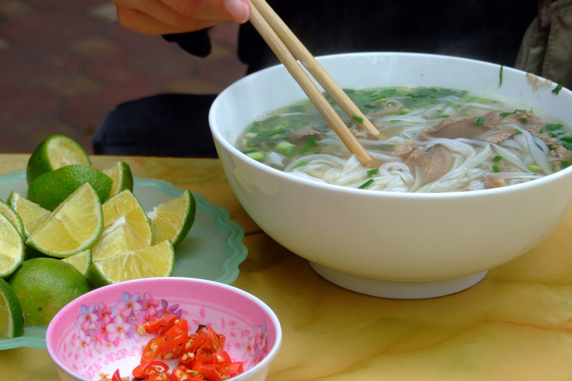 A bowl of phở bò with lime and chilli, photographed in Hanoi