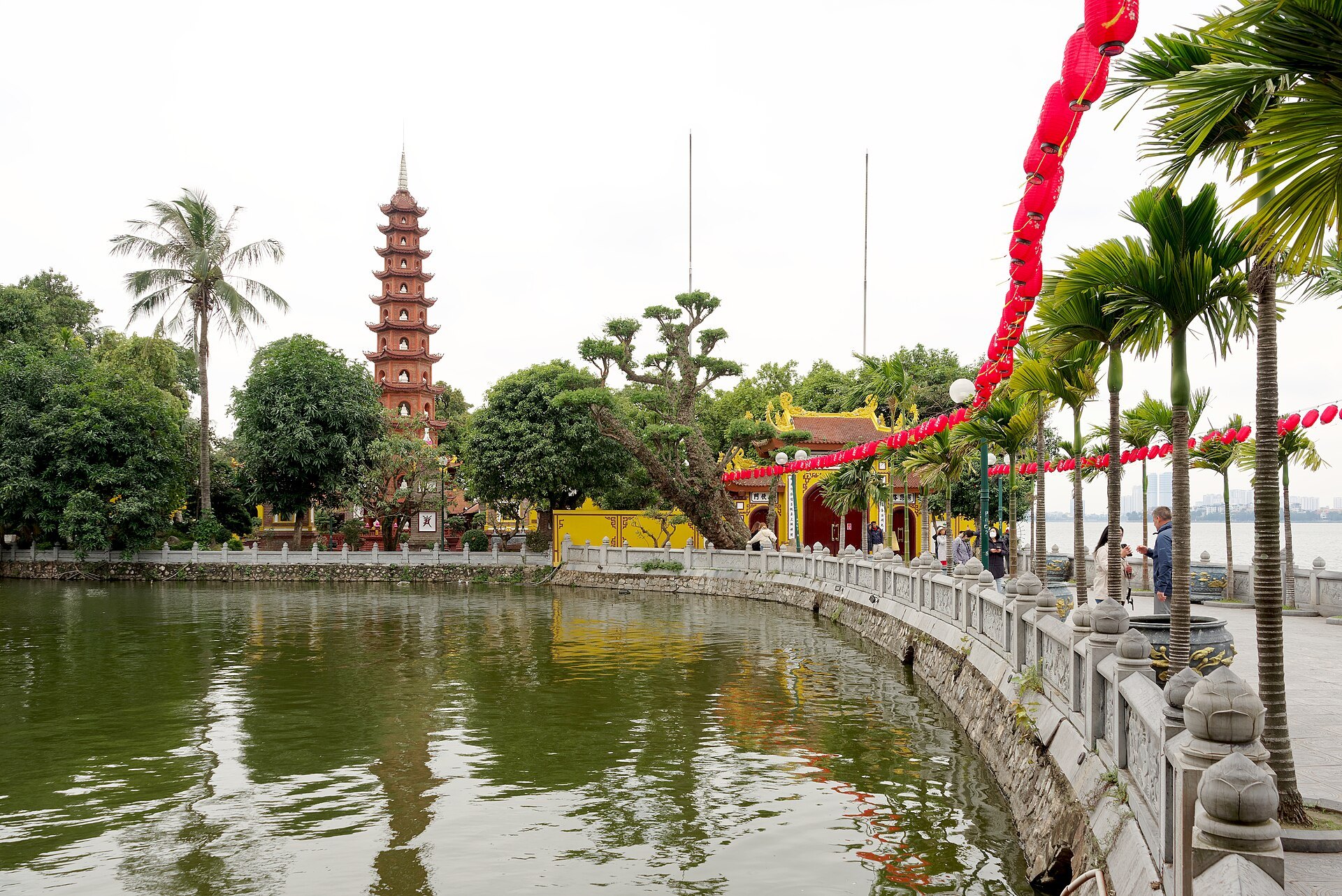 Tran Quoc Pagoda rising in red brick tiers above West Lake, with banners along the causeway